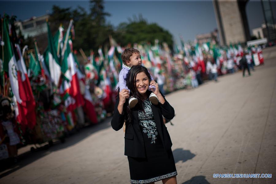 Una mujer cargaba su hijo pasando por puestos de decoración y banderas nacionales de México enfrente del monumento de Revolución el 1 de septiembre, en la Ciudad de México, capital de México, que va a celebrar el 205 aniversario de la independencia del país.