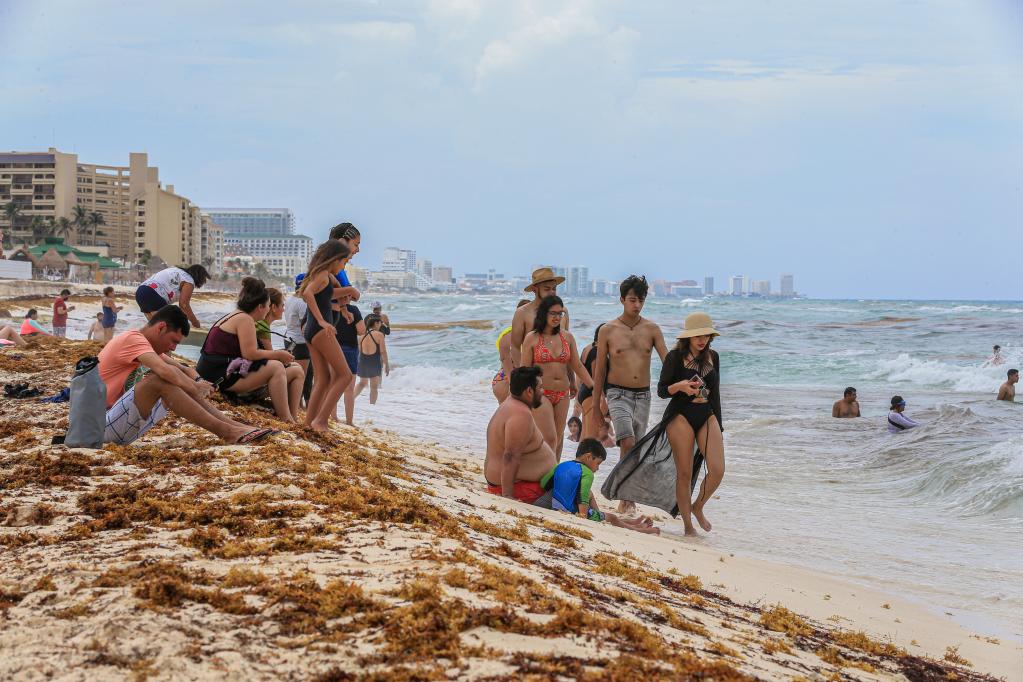 Personas disfrutan de su tiempo libre en medio del sargazo en playa Delfines en Cancún, México