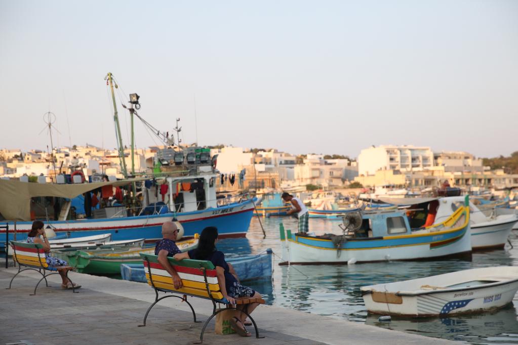Personas pasan el tiempo al atardecer en un puerto, Malta
